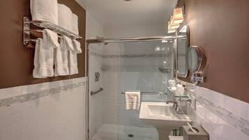 Un baño moderno con ducha de vidrio, tocador con espejo y toallero con varias toallas.