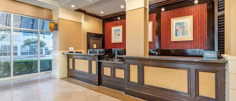 Een hotel receptie met een donker houten balie, een groot raam met uitzicht en een bord met de naam van het hotel.