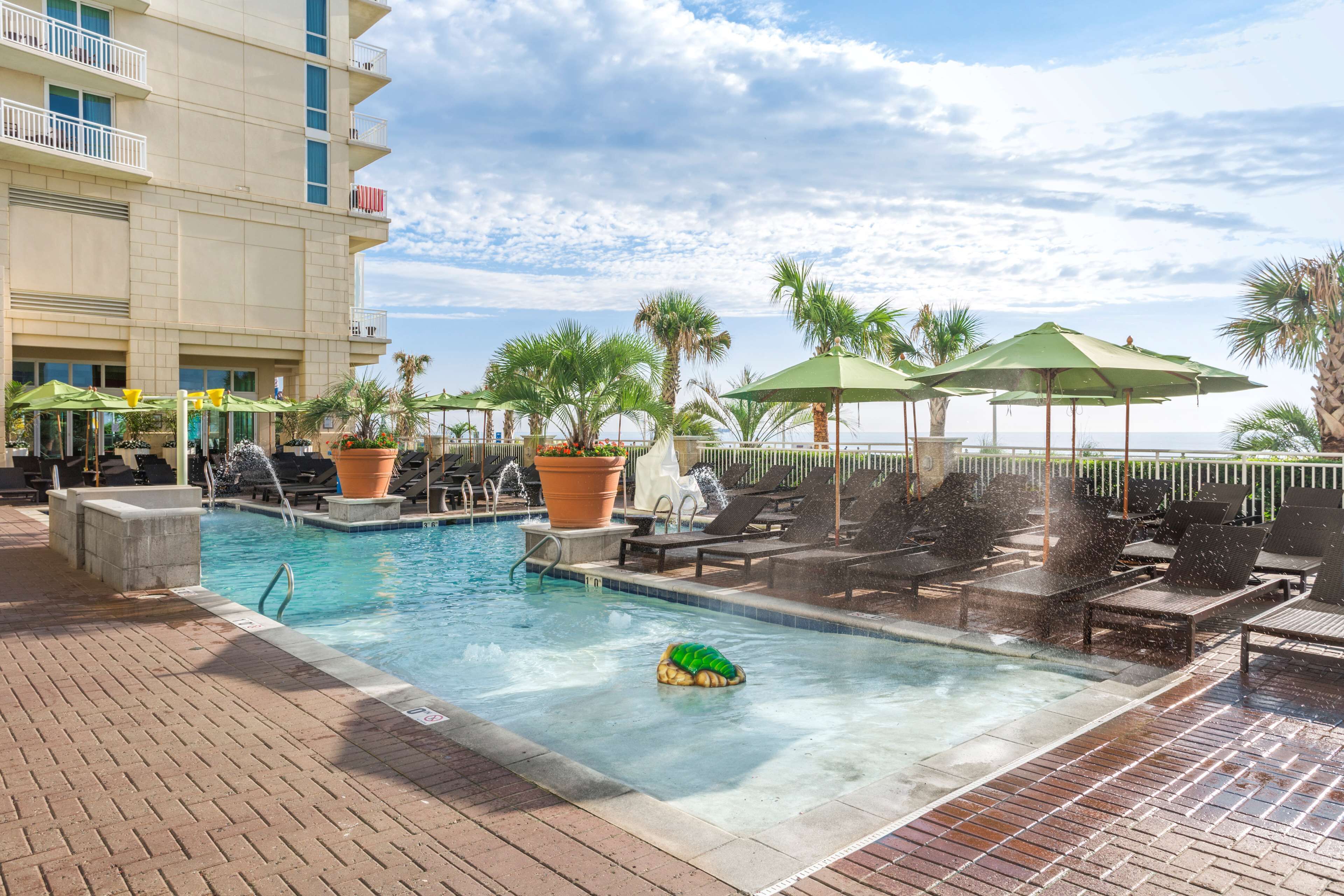 A pool area with lounge chairs and umbrellas, a water feature, and a building with balconies.