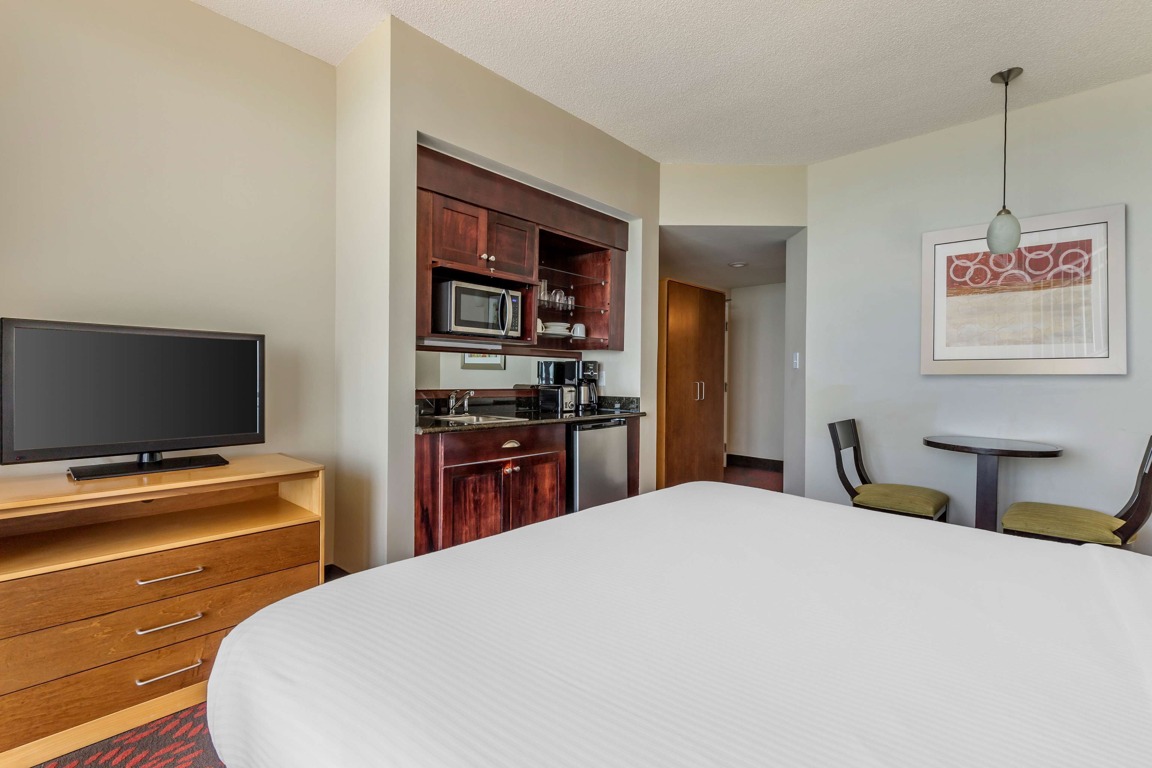 A hotel room with a bed, a TV, a kitchenette, and a small dining area.