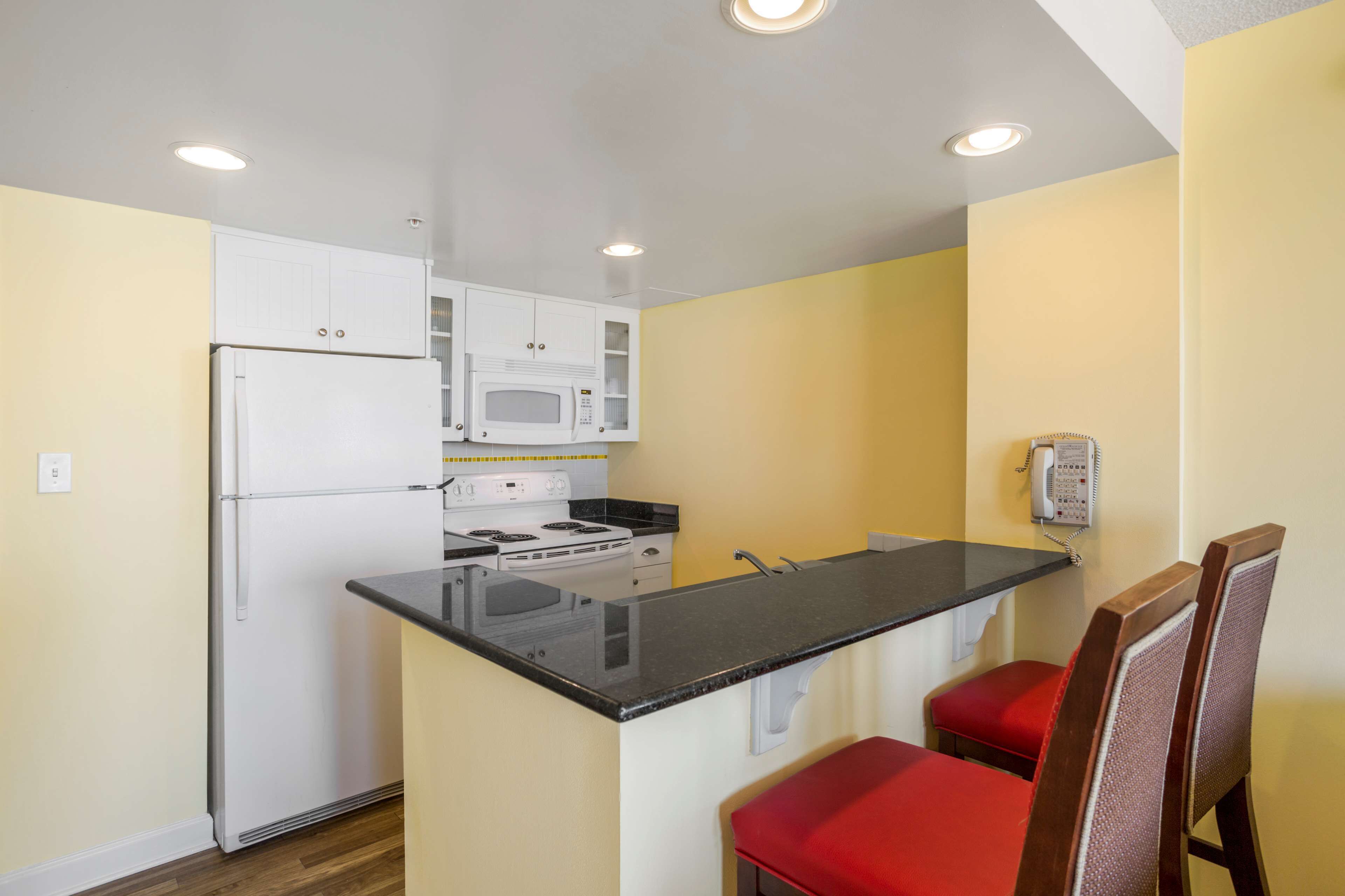 A compact kitchen with a refrigerator, microwave, stove, and a small dining area with red chairs.