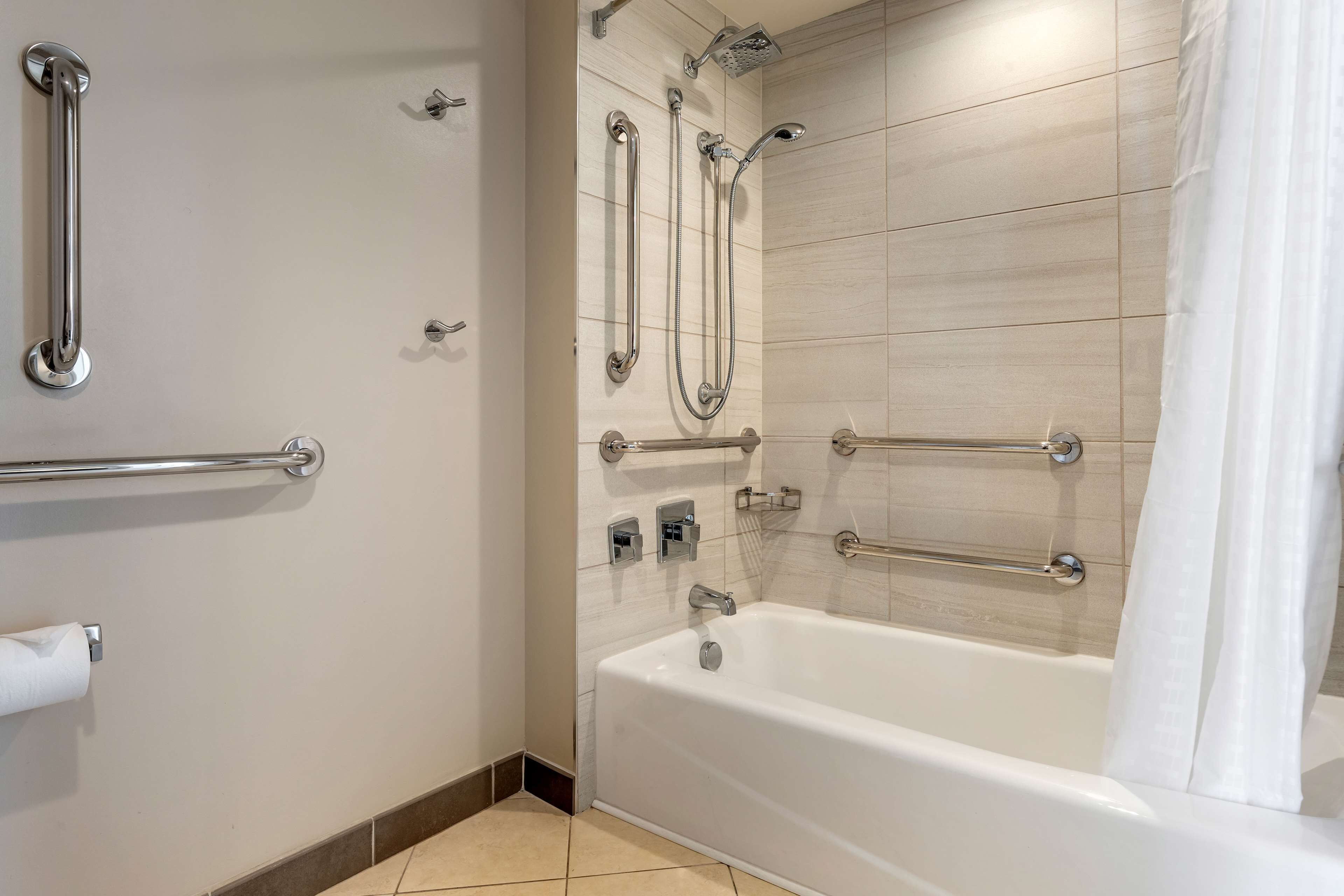 Un baño moderno con bañera, barras de apoyo y ducha con múltiples mandos.