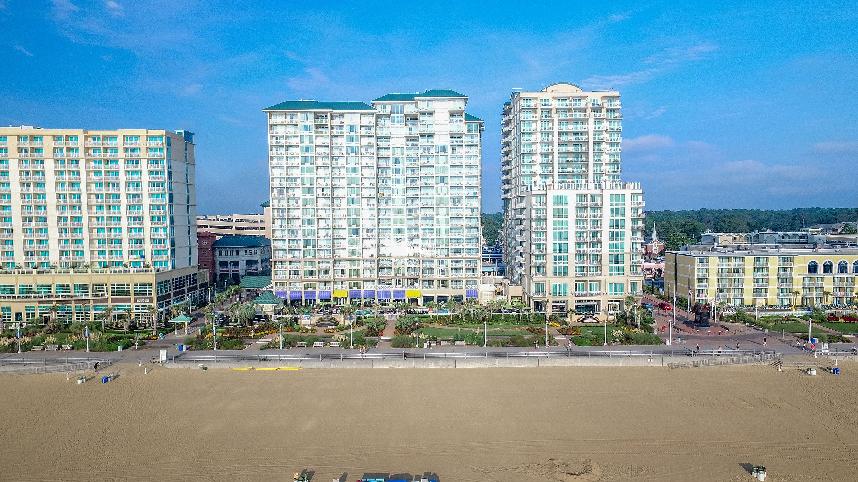 A high-rise hotel with multiple floors, a central courtyard, and a beach in the foreground.