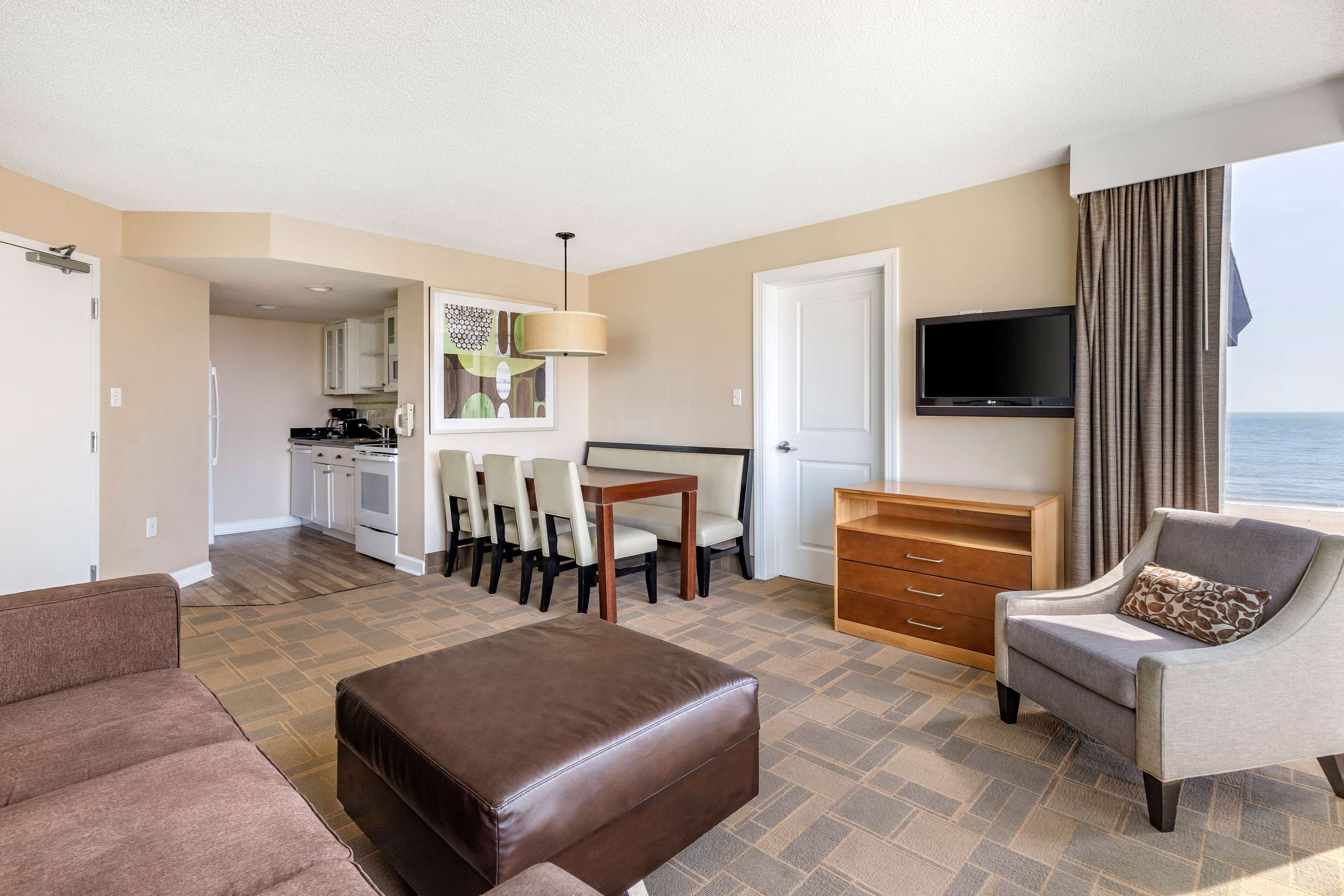 A hotel room with a living area, kitchenette, and a view of the sea.