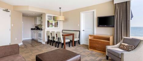 A hotel room with a living area, kitchenette, and a view of the sea.