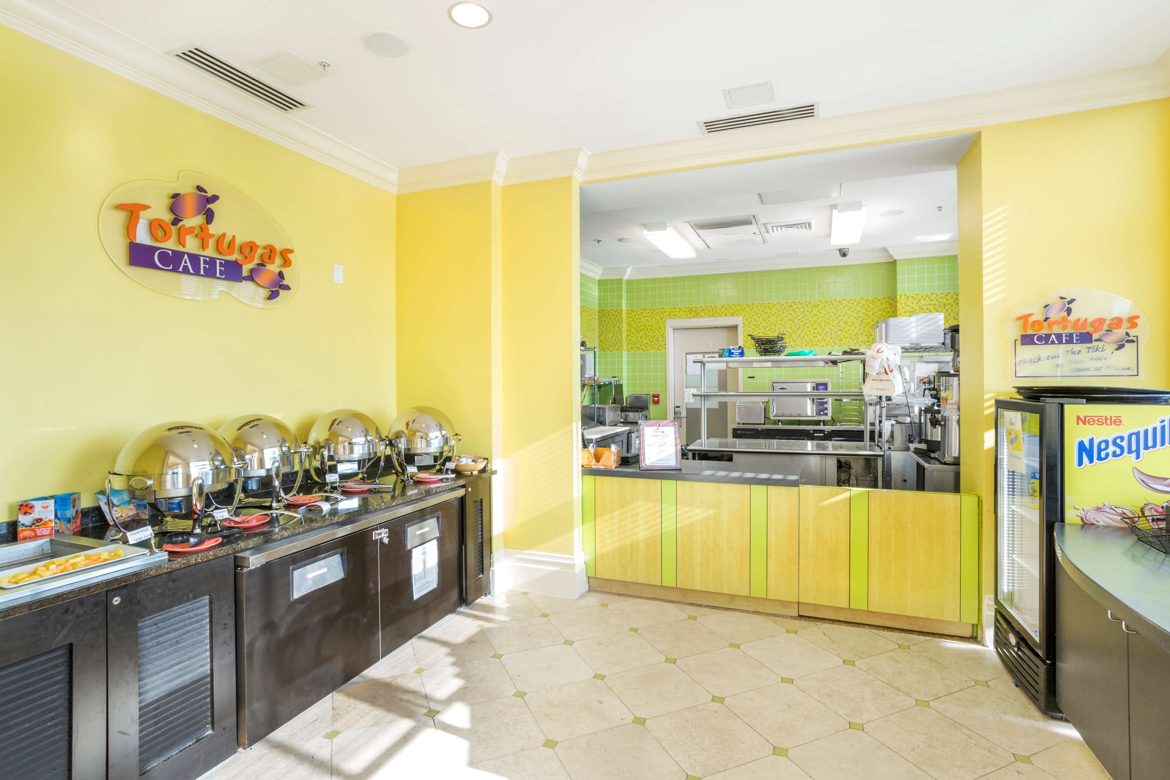 Un área de cocina luminosa de color amarillo y verde, con un letrero que dice 'Tortugas Cafe' y una presentación de Nestlé Nesquik.