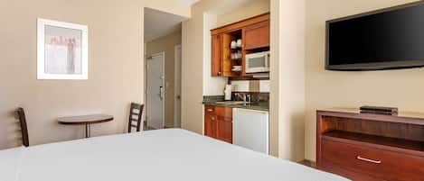Habitación de hotel con una cama grande, una pequeña mesa de comedor, una zona de cocina con microondas y un televisor de pantalla plana.