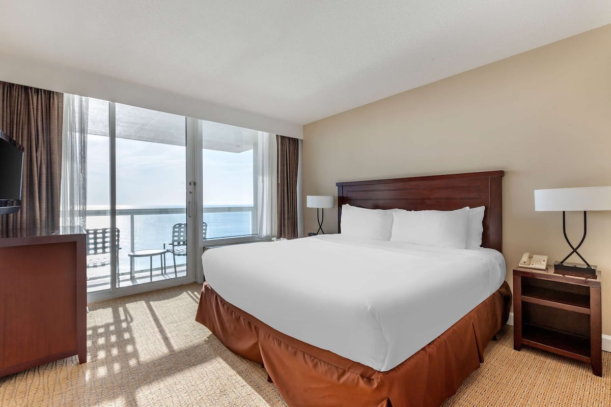 A hotel room with a large bed, a desk, a chair, and a balcony with a view.