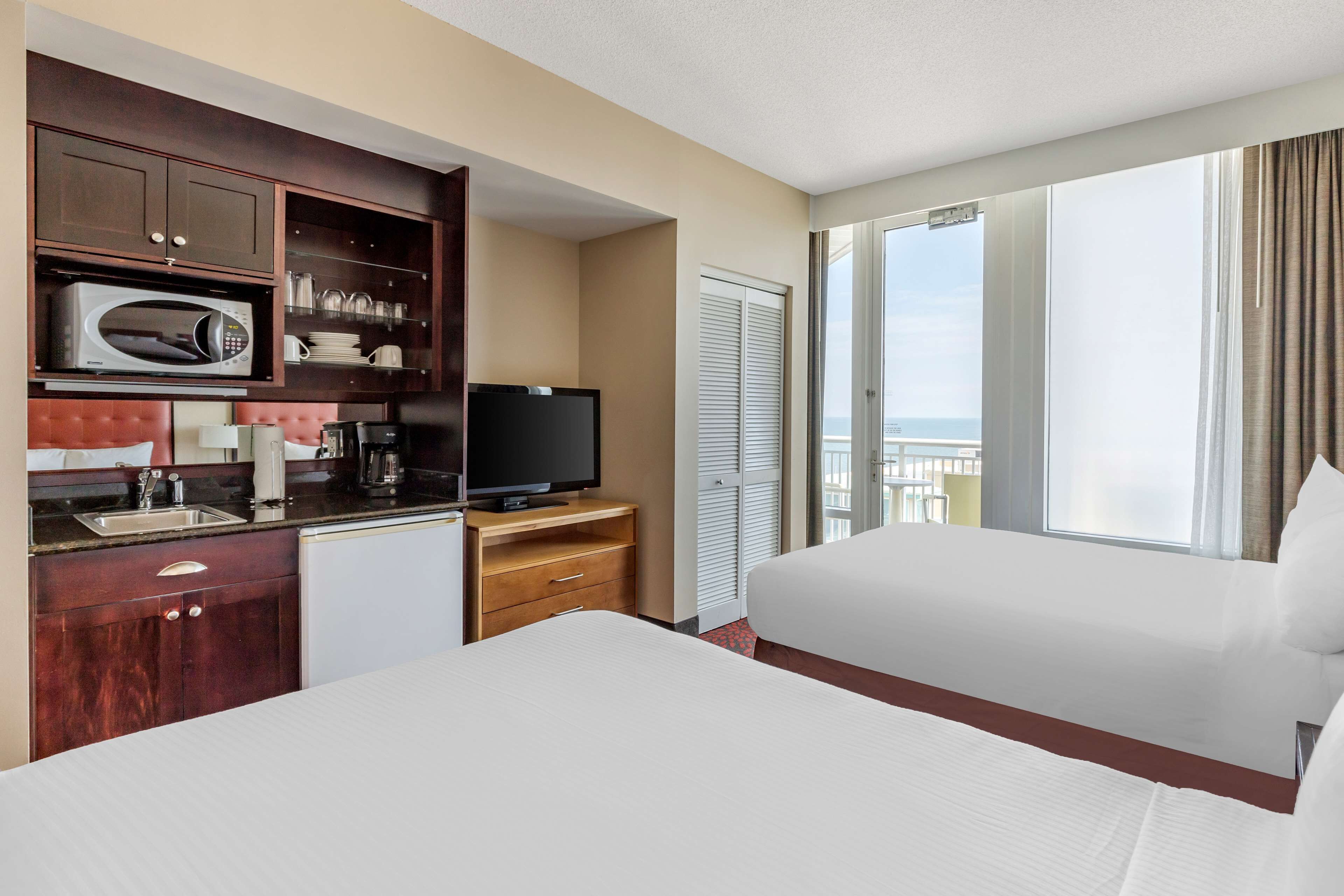 A hotel room with a kitchenette, a TV, a bed, and a balcony with a view.