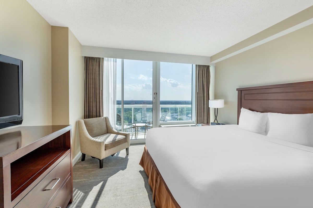 A hotel room with a large bed, a TV, a chair, and a balcony with a view.