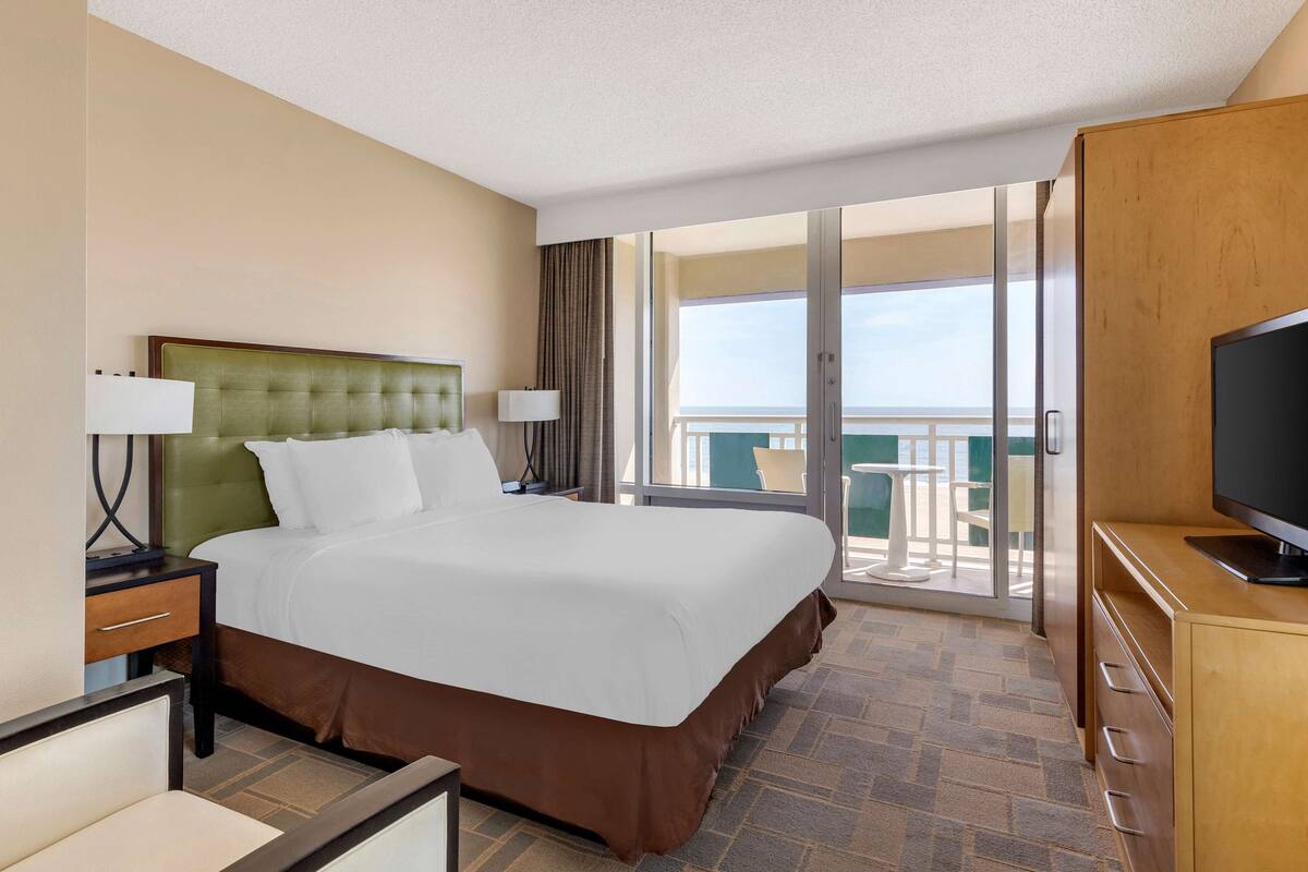 A hotel room with a large bed, a TV, a desk, and a balcony with a view.