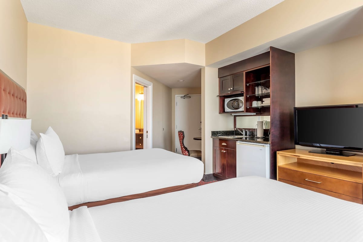 A hotel room with two beds, a TV, a microwave, and a small kitchenette.