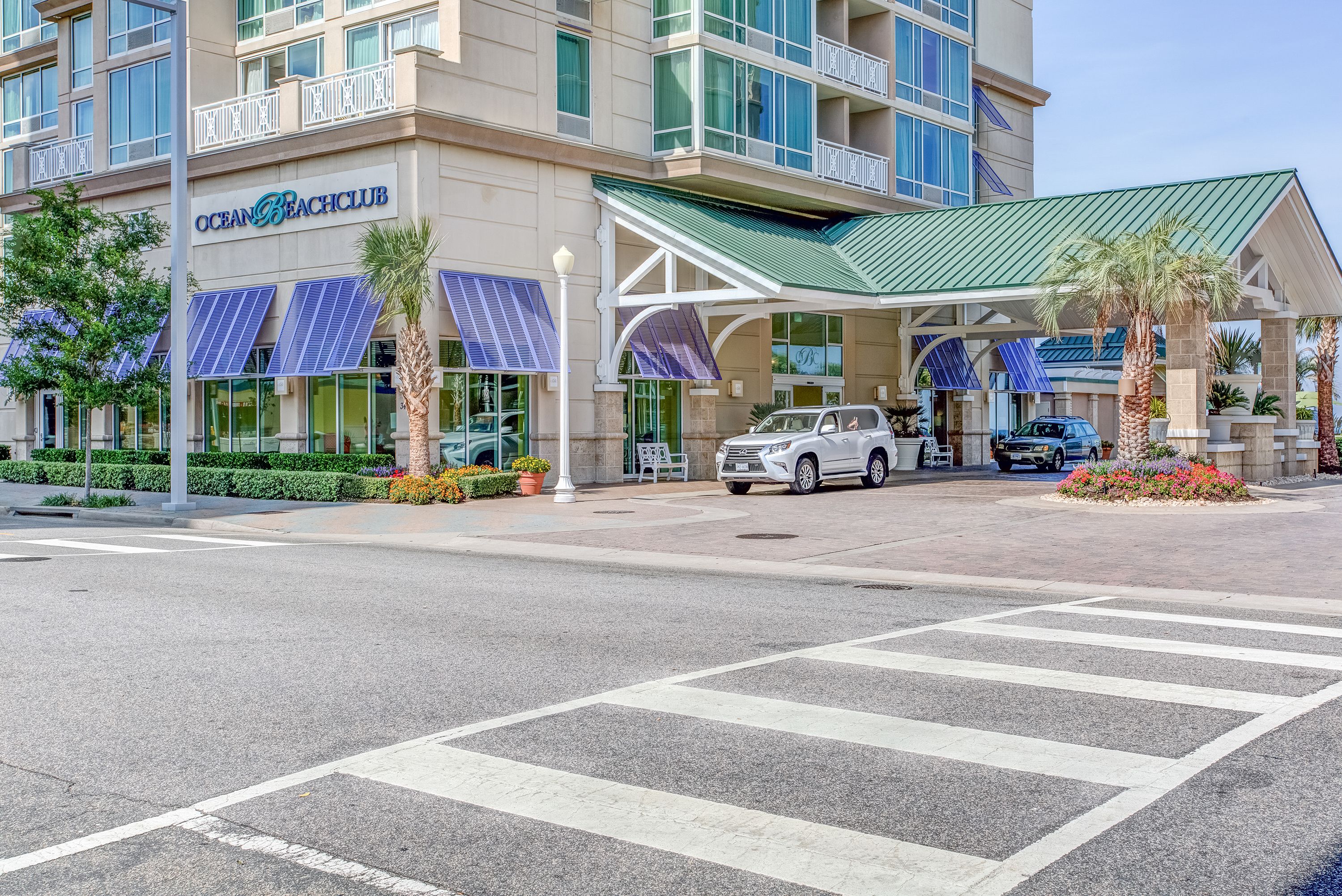 A hotel with a modern design, featuring a covered entrance, solar panels, and a landscaped area with palm trees.