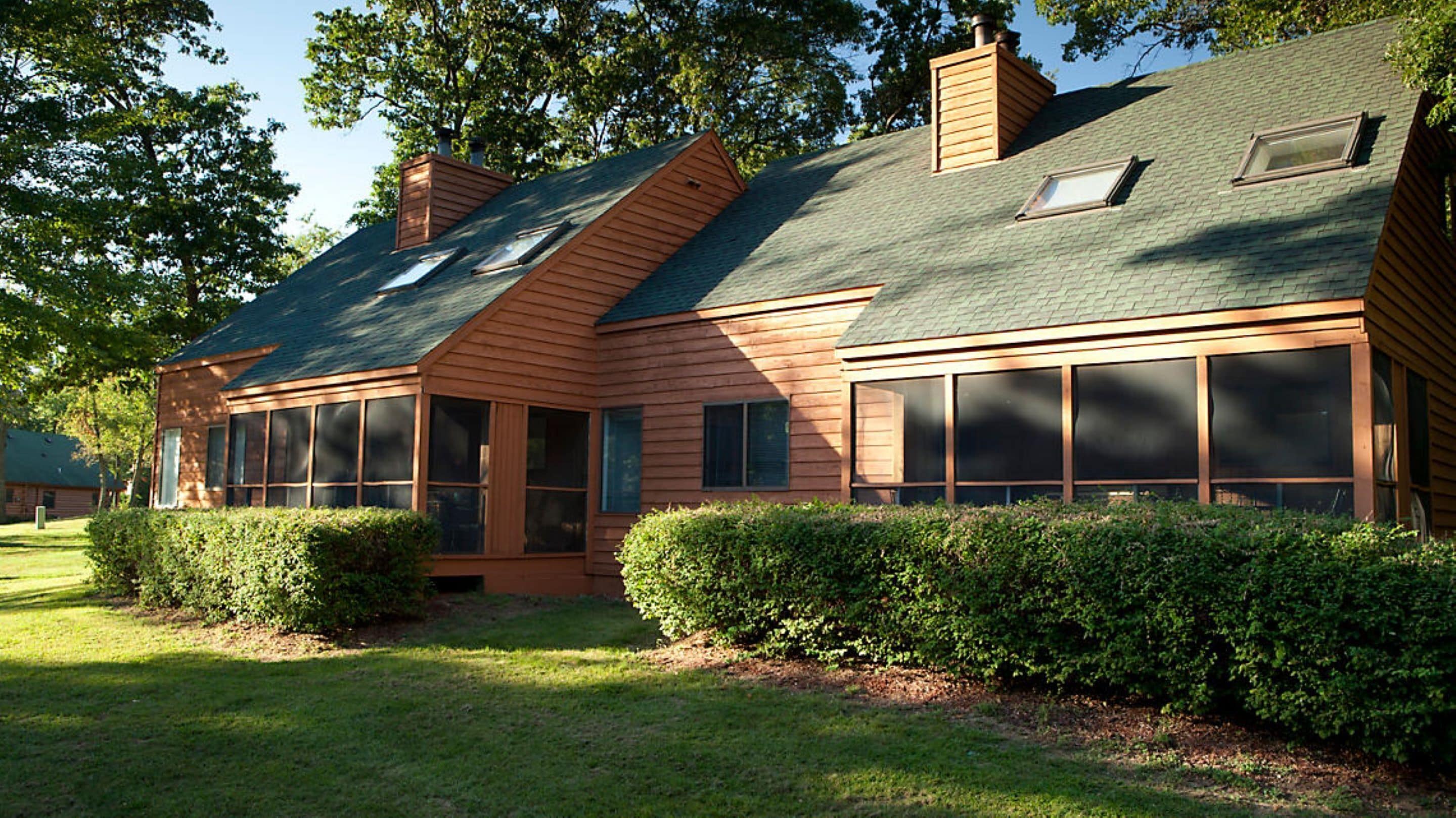 A wooden house with a sloped roof, large windows, and a well-maintained lawn.