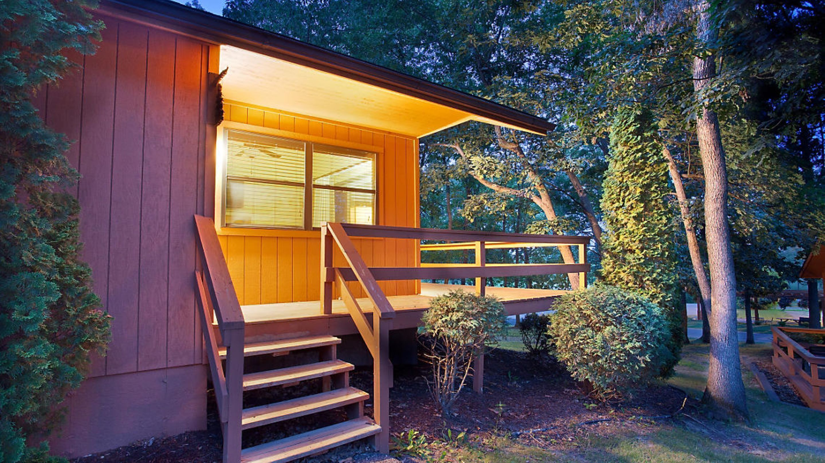 A wooden cabin with a porch, steps, and a window with blinds.