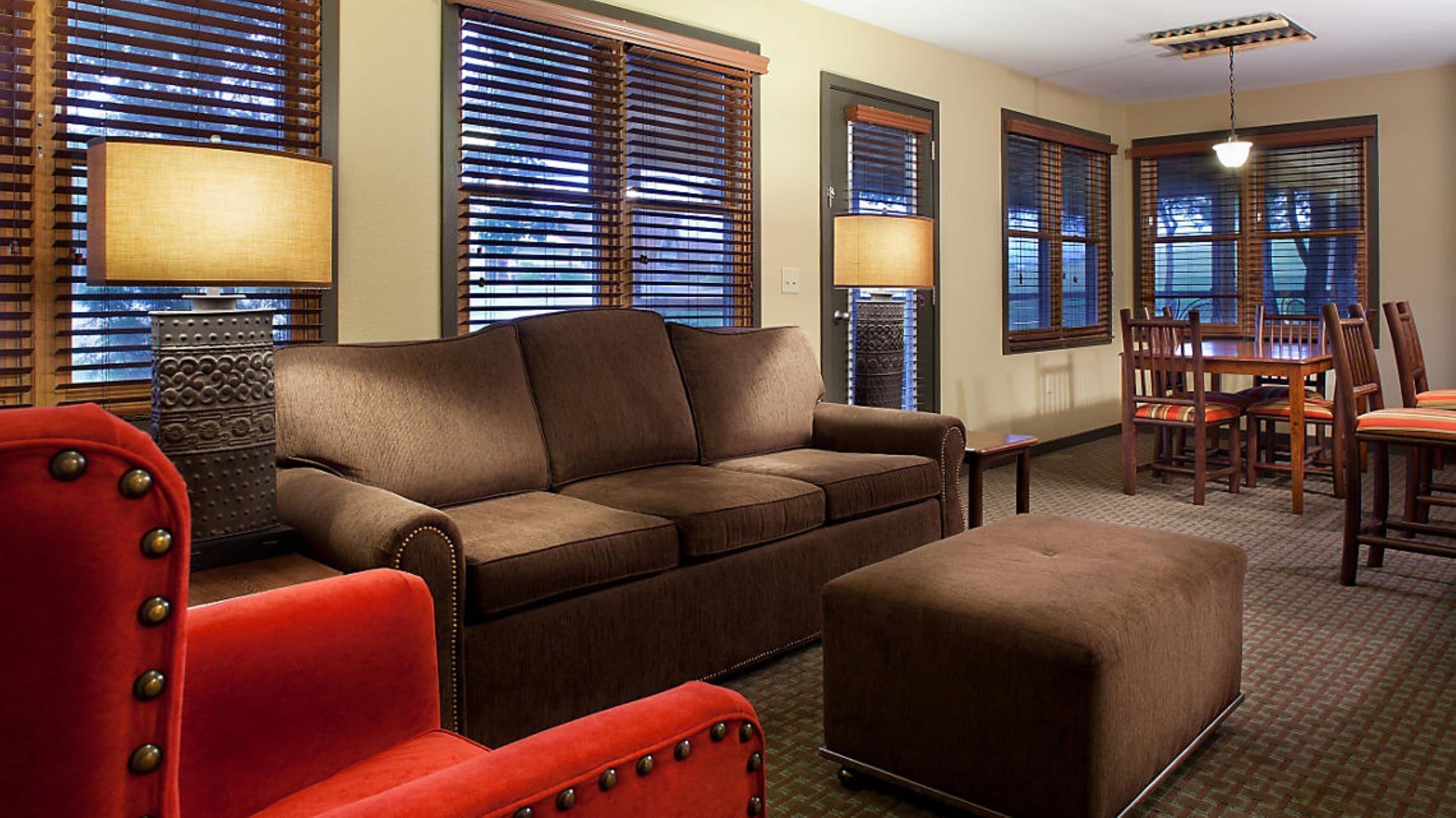 A living room with a brown sofa, a red armchair, a wooden dining table with chairs, and a patterned carpet.