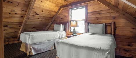 A room with two beds, wooden walls, a window with blinds, and a lamp.