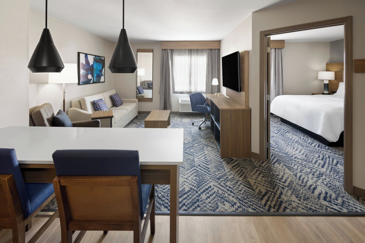 Een hotelkamer met een bed, bureau, stoel, bank, televisie en een groot raam.
