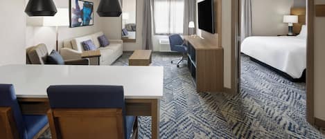 Et hotelværelse med seng, skrivebord, stol, sofa, fjernsyn og et stort vindue.
