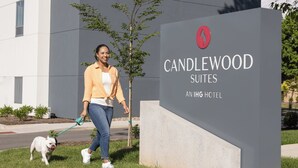 A woman walking a dog in front of a sign for Candlewood Suites, an IHG hotel.