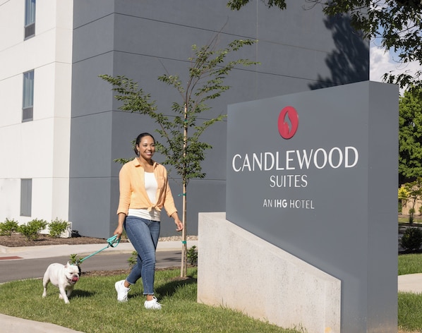Una mujer pasea un perro frente a un letrero de Candlewood Suites, un hotel IHG.