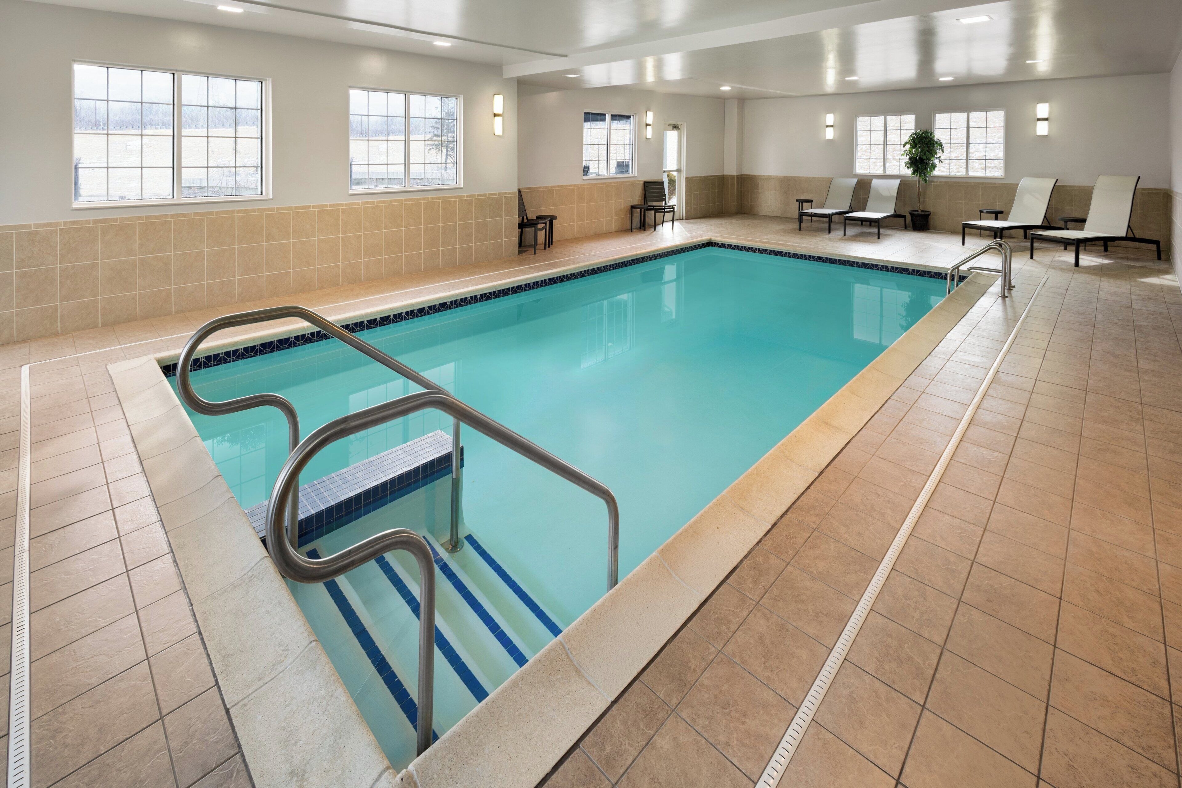 An indoor swimming pool with a tiled floor, a pool ladder, and several lounge chairs.