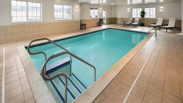 An indoor swimming pool with a tiled floor, a pool ladder, and several lounge chairs.