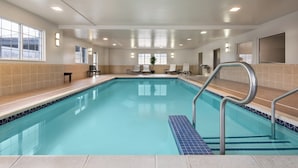 An indoor swimming pool with clear blue water, a tiled deck, and a few lounge chairs.