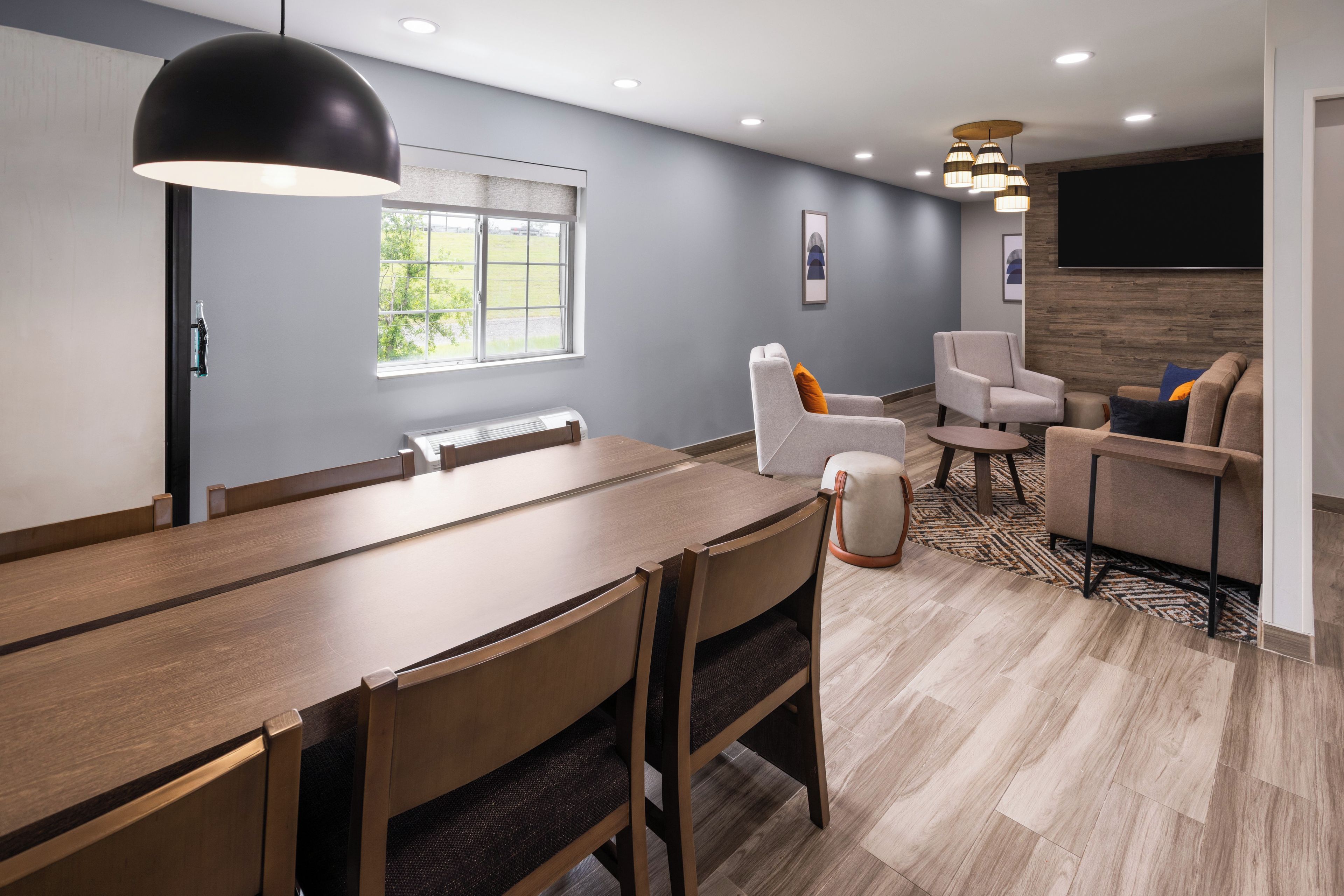 A modern dining area with a long wooden table, chairs, and a black pendant light.