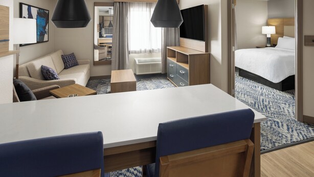 Ein Hotelzimmer mit Essbereich, einer Sitzecke, einem Fernseher, einem Bett und einem durch eine offene Tür einsehbaren Badezimmer.