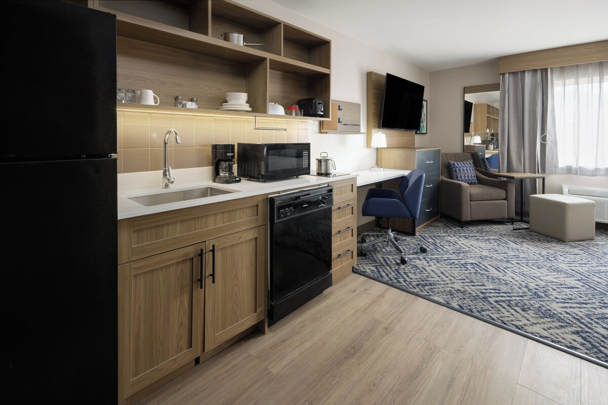 Een moderne keuken met een magnetron, koffiezetapparaat en vaatwasser. Er is een zithoek met een bank en fauteuil, en een flatscreen-tv aan de muur bevestigd.