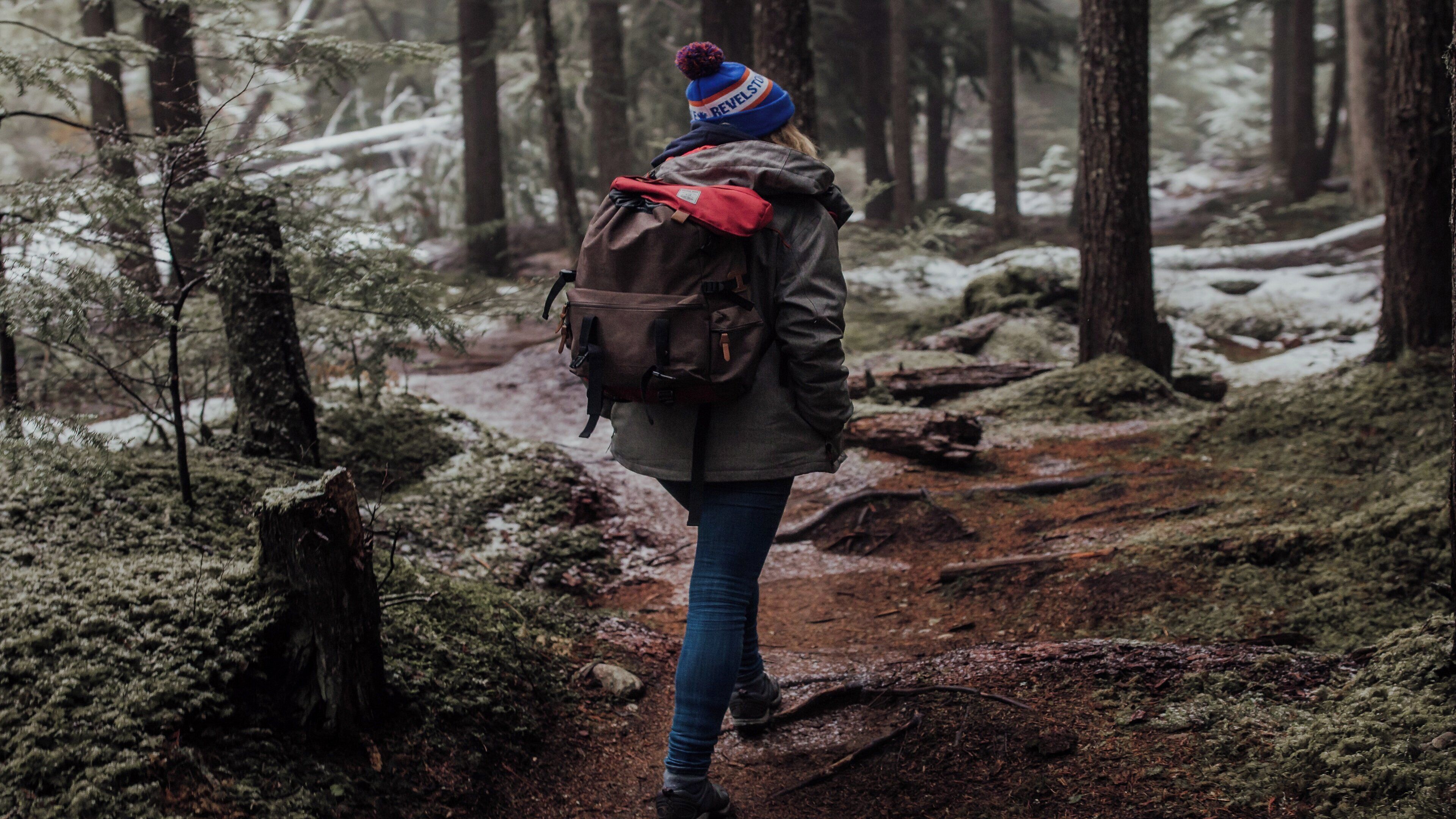 A person walking on a forest trail with moss-covered trees and a backpack.