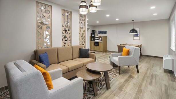 A modern living area with a sofa, armchairs, a coffee station, and a dining table.