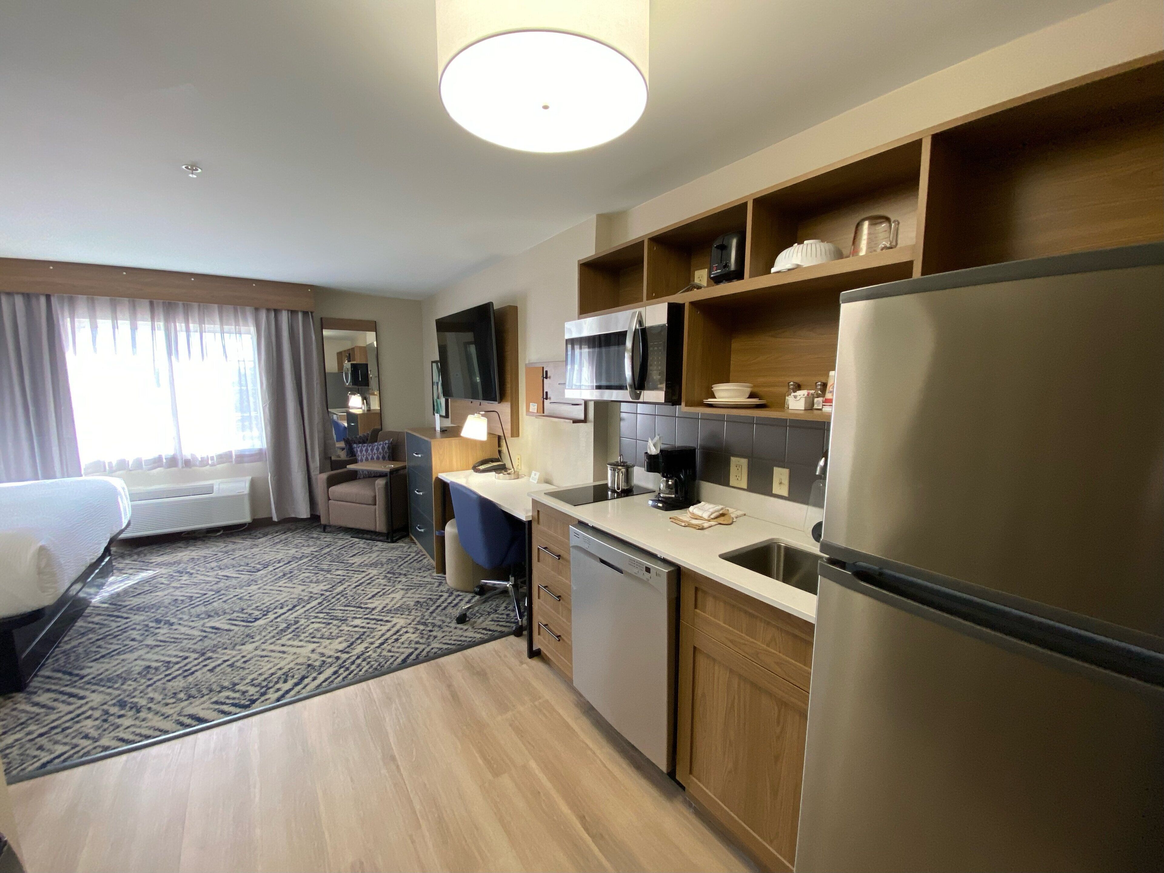 A hotel room with a bed, a desk, a chair, a microwave, a refrigerator, and a small kitchenette.