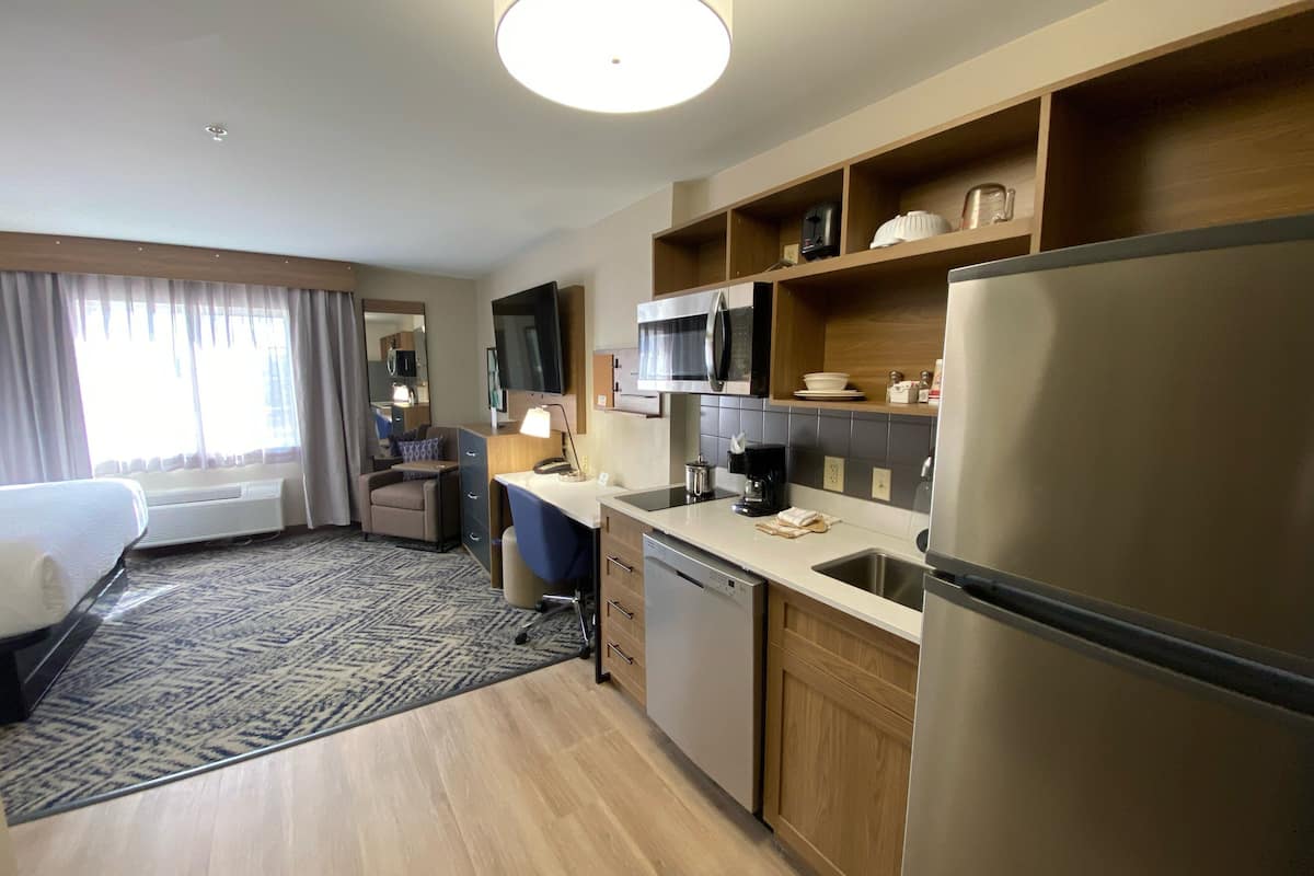 Ein Hotelzimmer mit Bett, Schreibtisch, Stuhl, Mikrowelle, Kühlschrank und einer kleinen Küchenzeile.