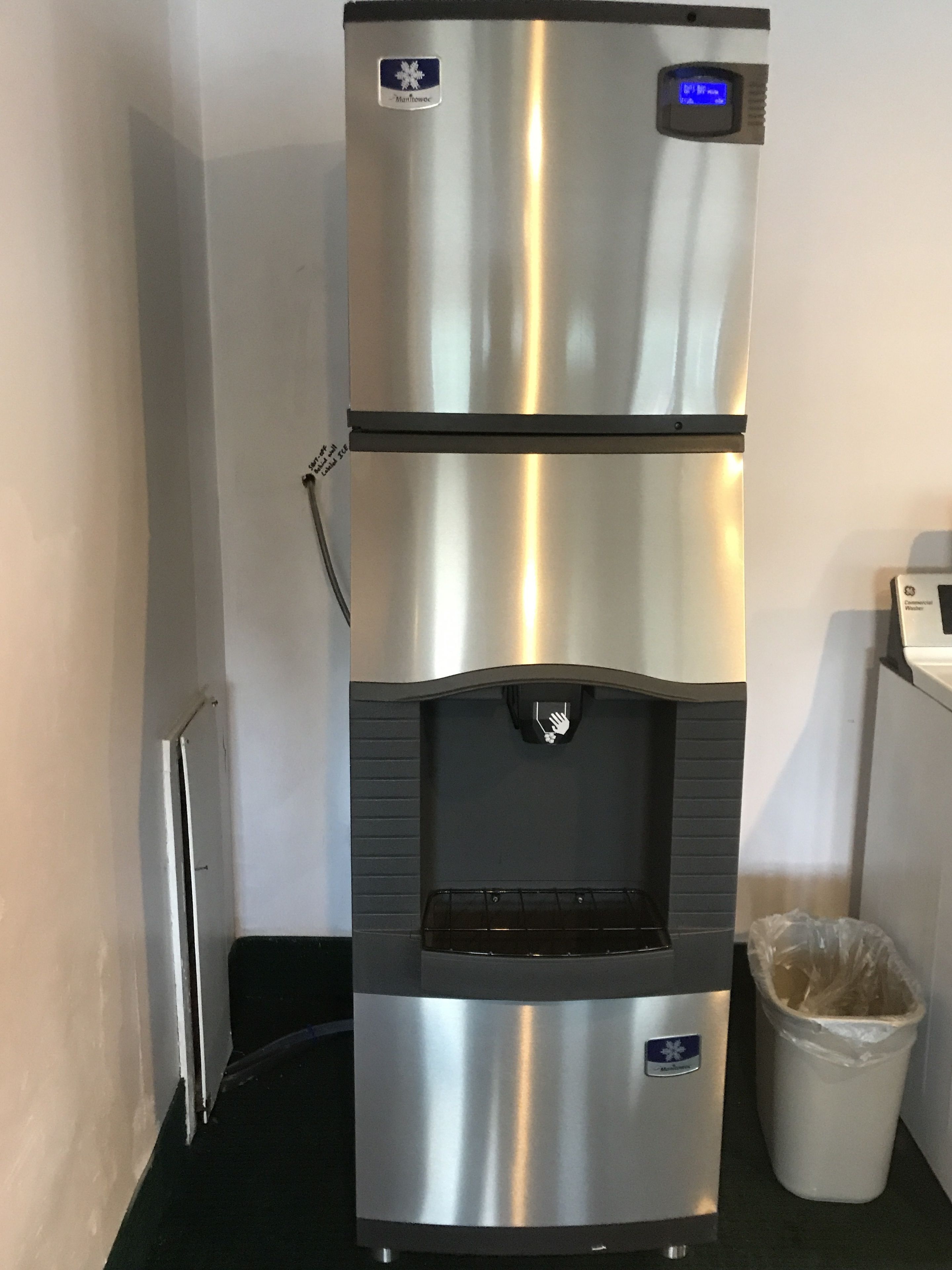 A stainless steel commercial refrigerator with a water dispenser and a trash bin.