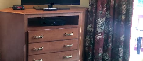 A television on a wooden cabinet with drawers, a remote control, and a clock.