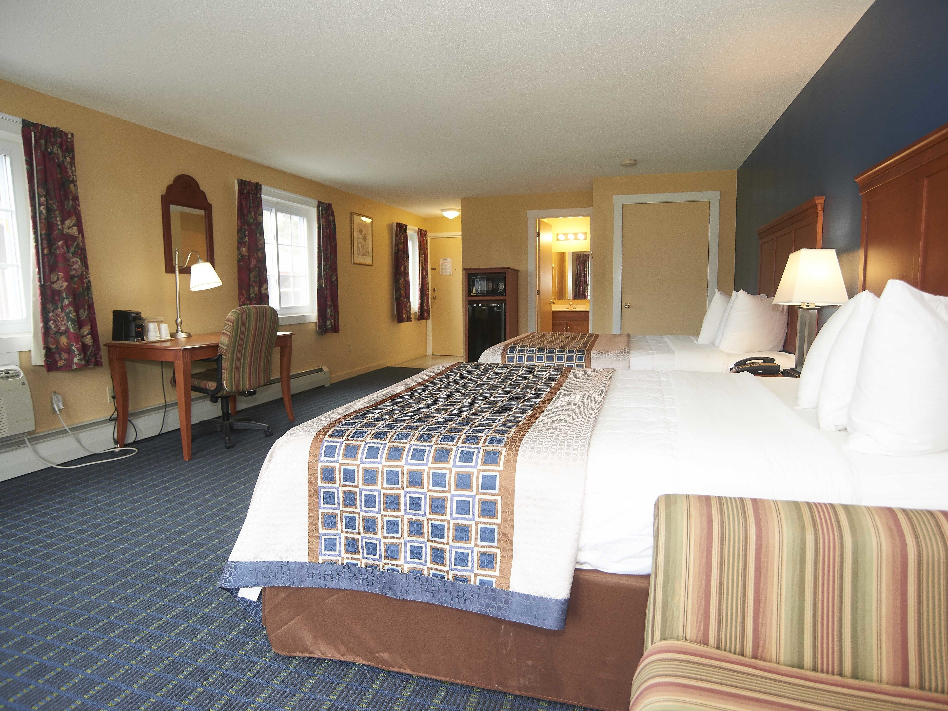 A hotel room with a large bed, a desk with a lamp, a chair, and a bathroom visible through an open door.