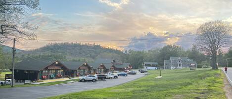 A row of log cabins with a parking lot in front, a grassy area, and a hilly backdrop.