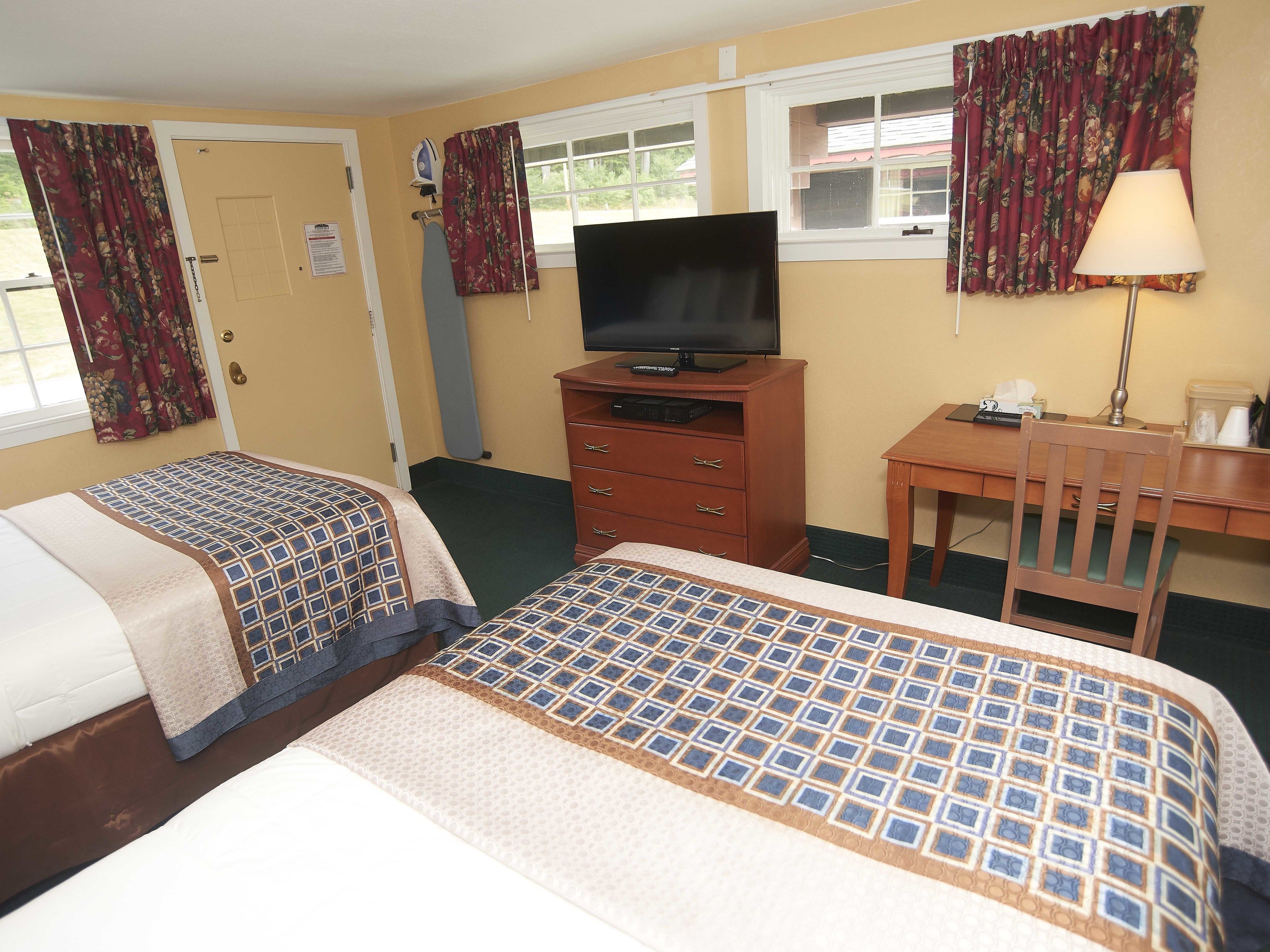 Habitación de hotel con dos camas, un televisor sobre un mueble de madera, un escritorio con una silla y una ventana con cortinas.