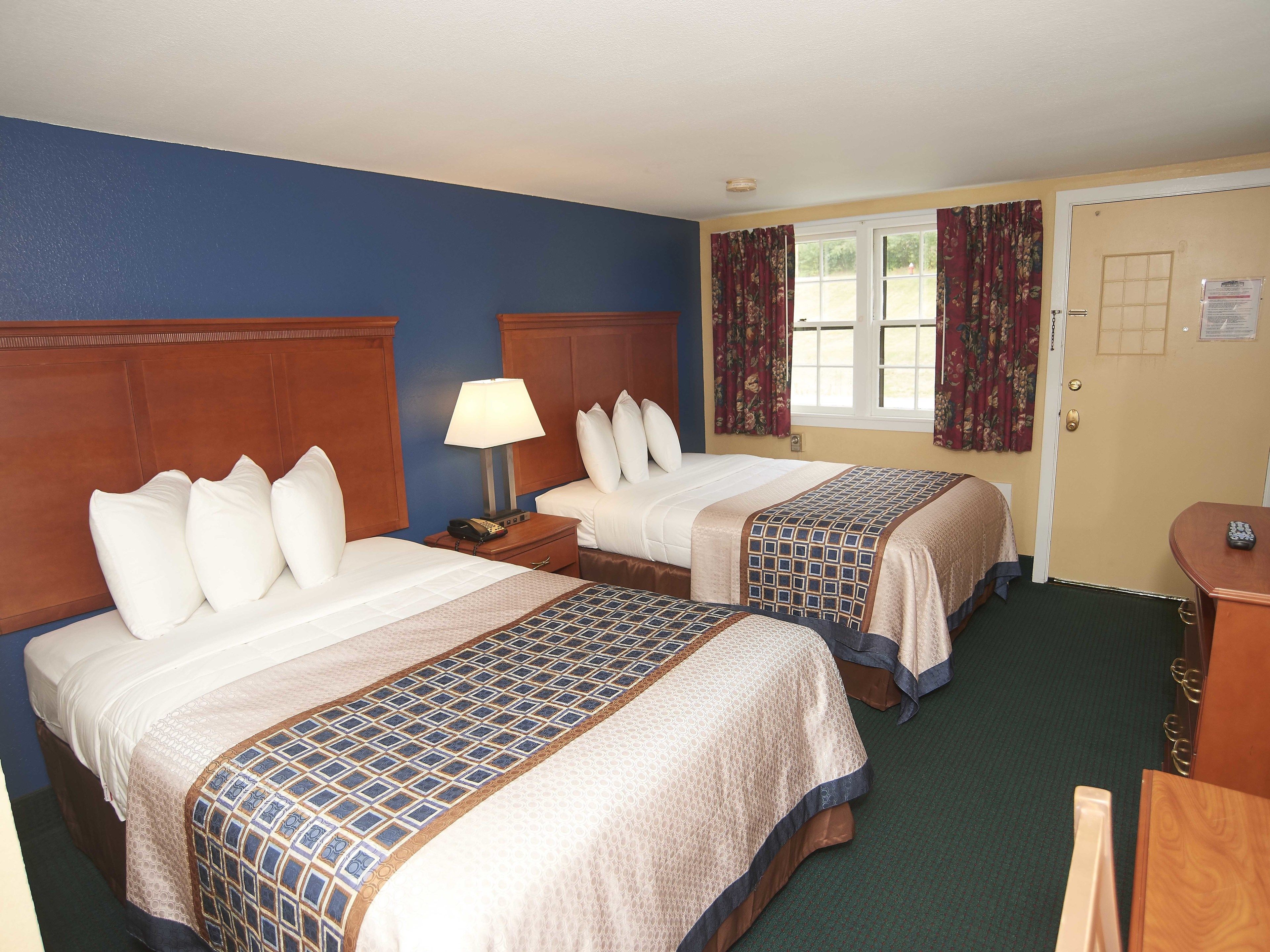 Habitación de hotel con dos camas, una mesita de noche con lámpara, un escritorio y una puerta con ventana y cortinas.