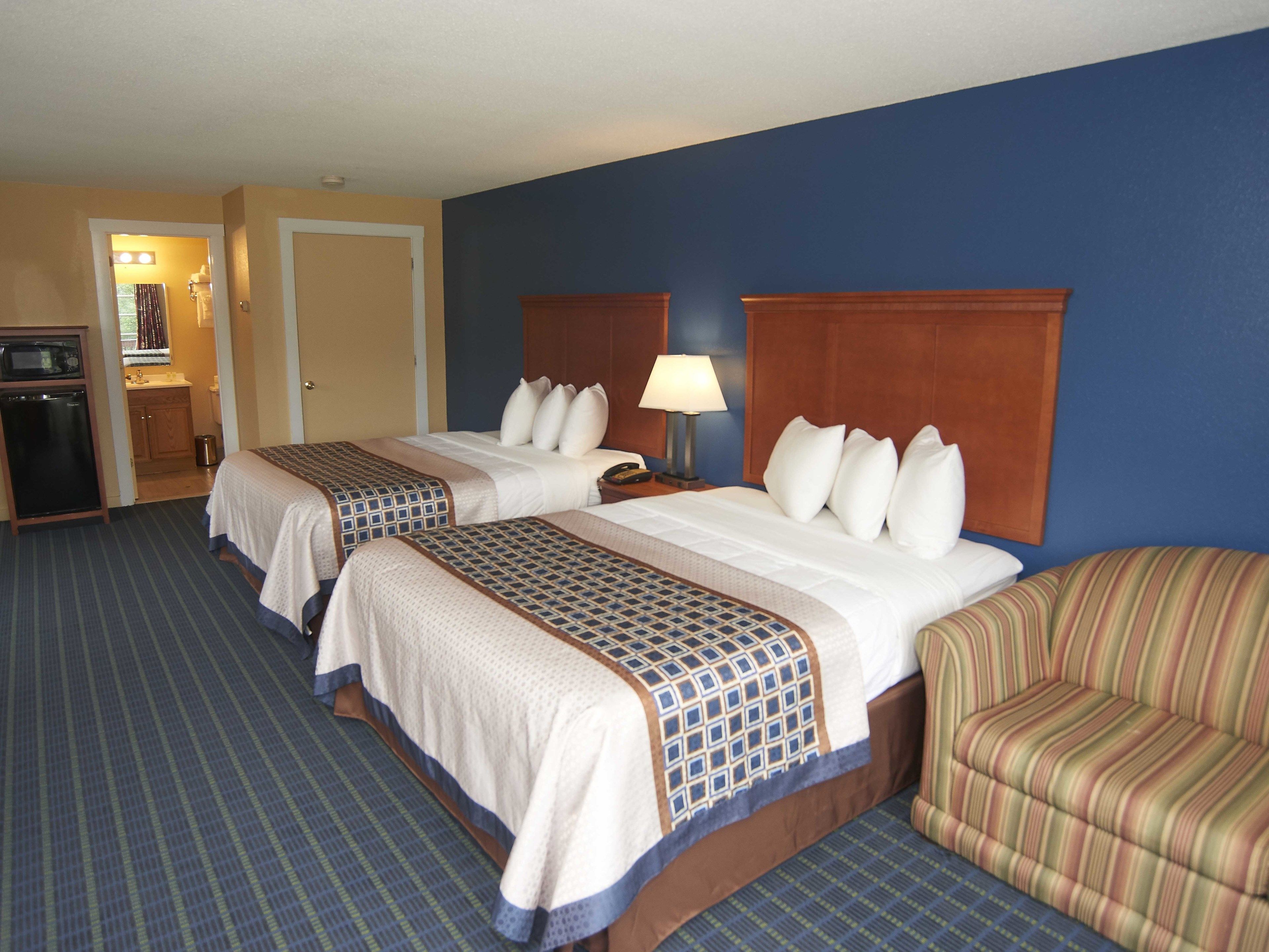 A hotel room with two beds, a desk, a chair, a microwave, and a small kitchenette.