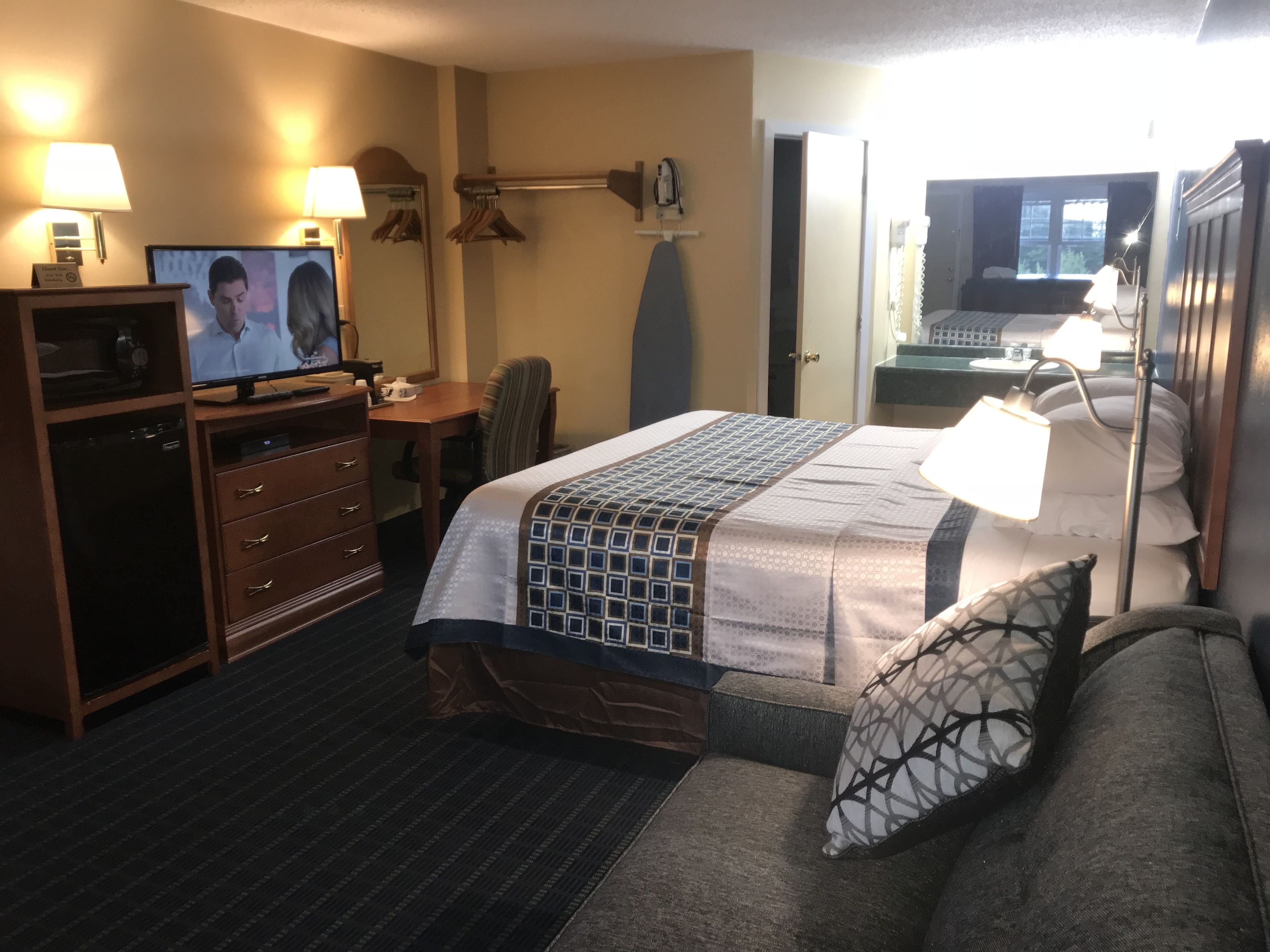 A hotel room with a bed, a desk, a television, a dresser, and a bathroom visible through an open door.