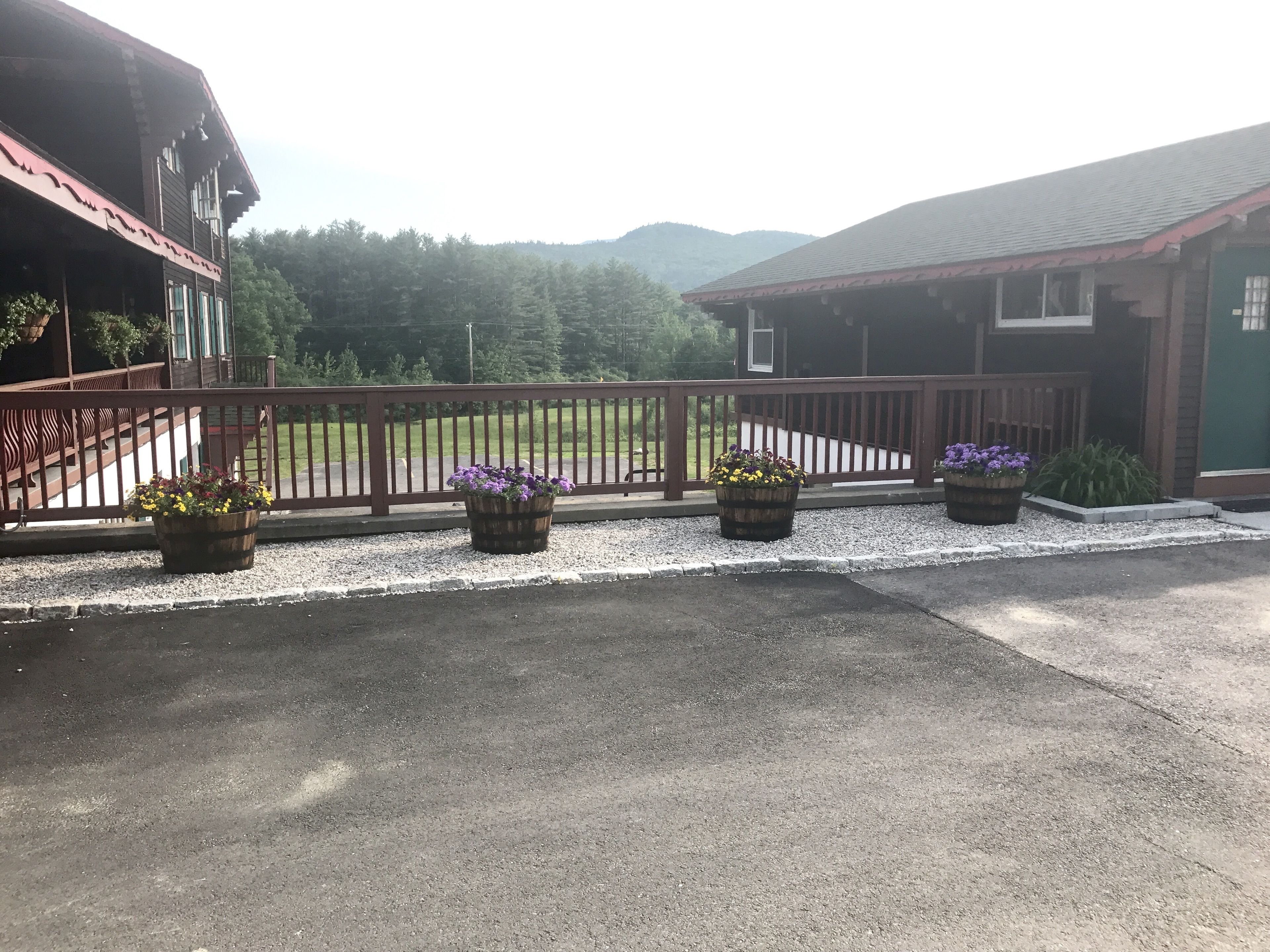 A building with a wooden deck and a gravel pathway. There are three flower planters along the pathway.