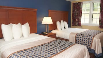 Camera d'albergo con due letti, ognuno con testiera in legno, biancheria da letto bianca e copriletto decorato. Tra i letti si trova un comodino con una lampada e un telefono.