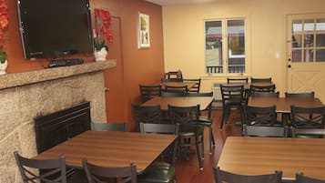 A dining area with tables and chairs, a fireplace, a television, and a window with a view of the outside.