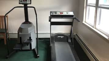 Un gimnasio con cintas de correr y una bicicleta estática, suelo alfombrado y una ventana con vistas.
