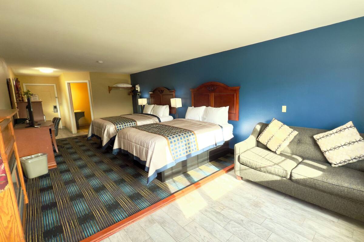 A hotel room with two beds, a sofa, a desk, and a trash bin.
