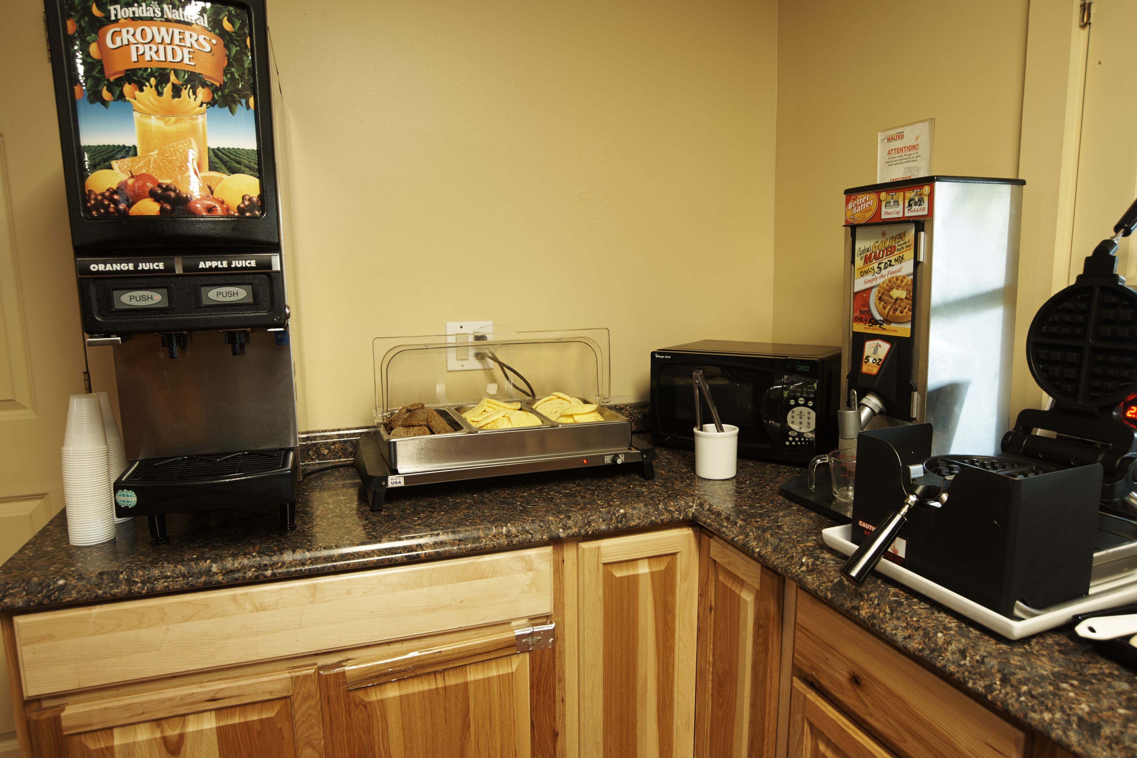 A breakfast bar with juice dispensers, a waffle maker, and a coffee maker.