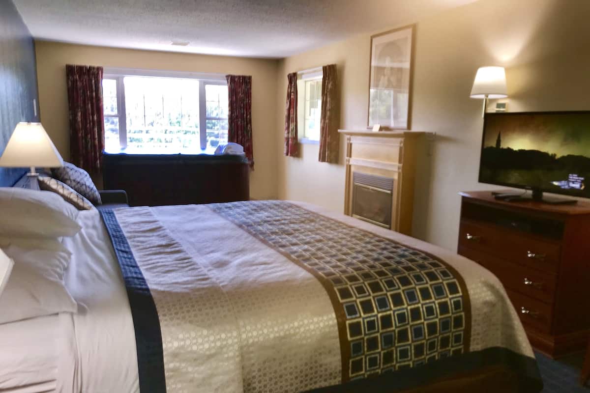 A hotel room with a large bed, a television on a wooden cabinet, a fireplace, and a window with curtains.